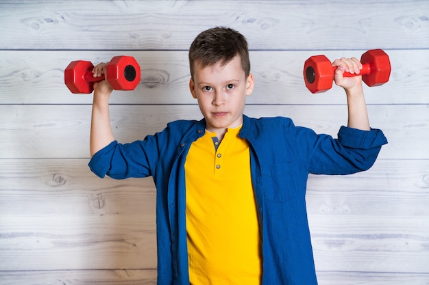 Young boy in casual clothes with dumbbells