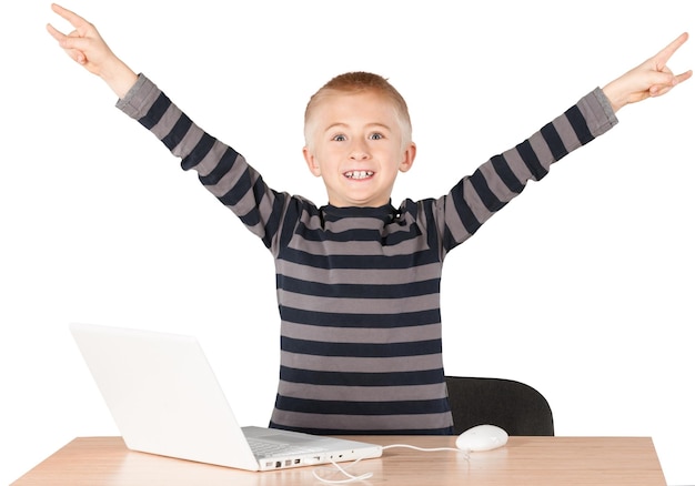 Молодой мальчик празднует с распростертыми объятиями над ноутбуком на столе
