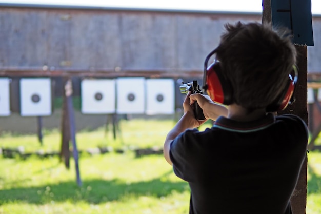 Photo young boy concentrates while shooting from a revolver at a shooting range