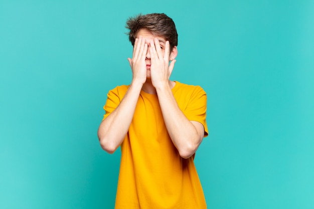 Young boy covering face with hands, peeking between fingers with surprised expression and looking to the side