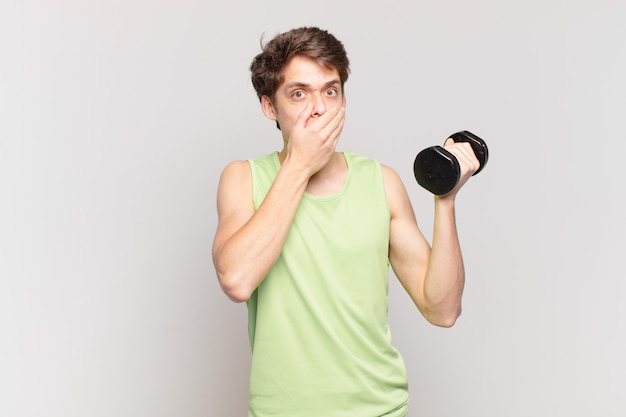 Young boy covering mouth with hands with a shocked, surprised expression, keeping a secret or saying oops. dumbbell concept