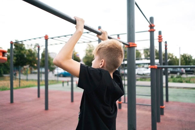 A young boy doing pull-ups outdoors, sport fitness exercise practice