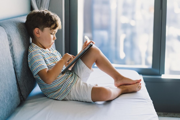 Young boy engrossed in playing tablet on a cozy couch during afternoon hours
