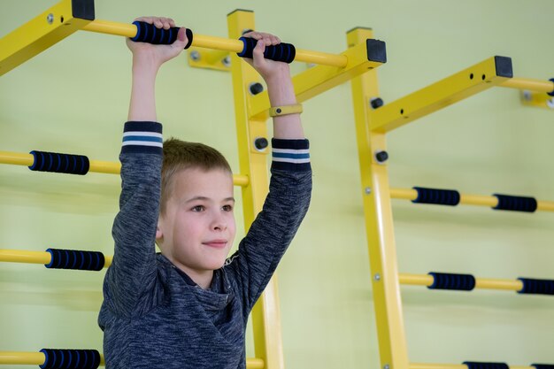 Young boy exercising on a wall ladder bar inside sports gym