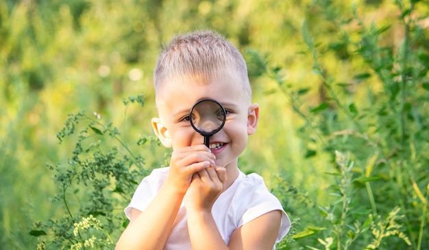 Young boy exploring nature in the meadow with a magnifying glass looking at flowers Curious children in the woods