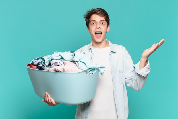 Young boy feeling happy, excited, surprised or shocked, smiling and astonished at something unbelievable washing clothes concept
