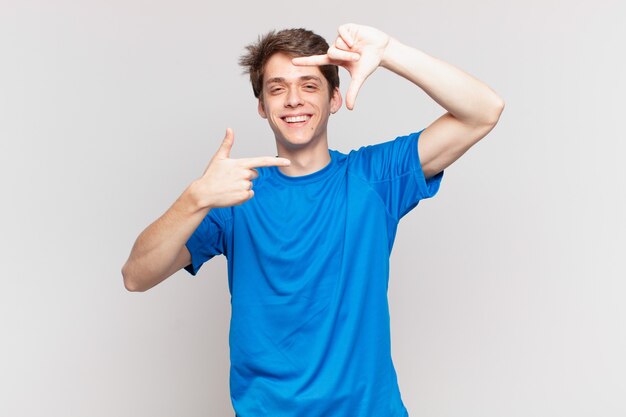 Young boy feeling happy, friendly and positive, smiling and making a portrait or photo frame with hands