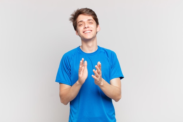 Young boy feeling happy and successful, smiling and clapping hands, saying congratulations with an applause