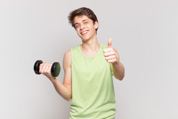 Young boy feeling proud, carefree, confident and happy, smiling positively with thumbs up. dumbbell concept