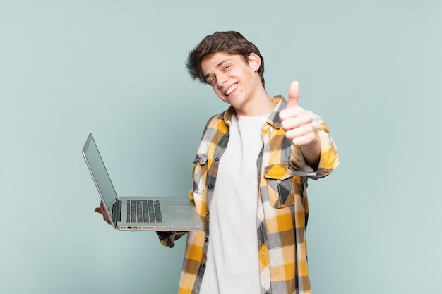 Young boy feeling proud, carefree, confident and happy, smiling positively with thumbs up. laptop concept
