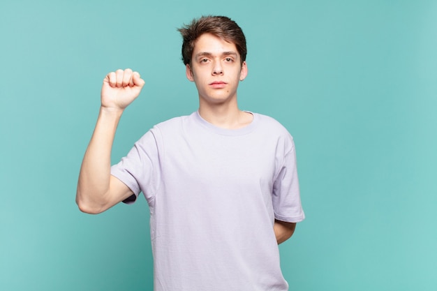 Young boy feeling serious, strong and rebellious, raising fist up, protesting or fighting for revolution