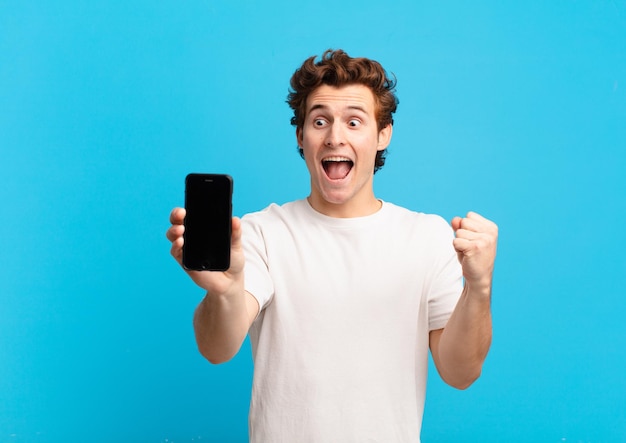 Ragazzo che si sente scioccato, eccitato e felice, ride e celebra il successo, dicendo wow!. concetto di schermo del telefono