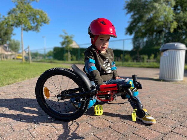 Photo young boy of four with disappointed face by learning bicycle on street