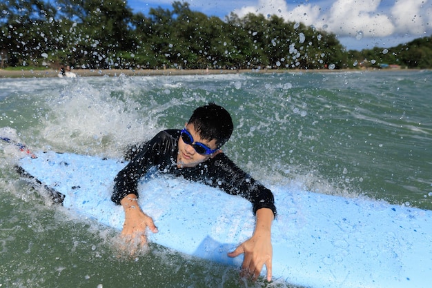 Un giovane ragazzo una matricola nel surf si sta aggrappando al softboard e sta cercando di riportarlo in mare per esercitarsi mentre gioca contro le onde e gli schizzi d'acqua