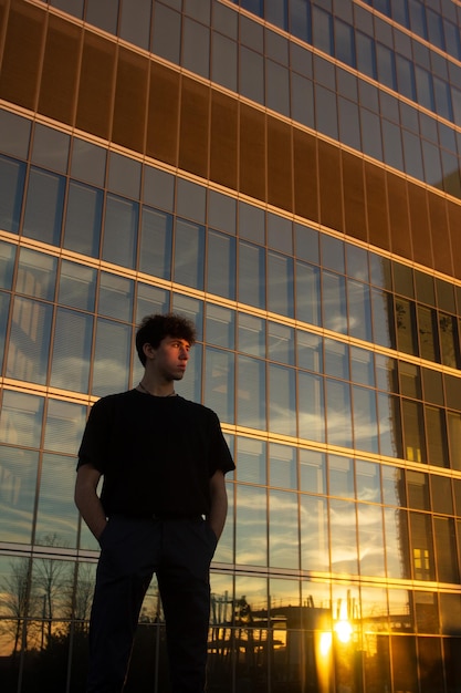 Ragazzo davanti all'edificio per uffici nella luce della sera guardando lo skyline