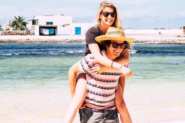 Young boy and girl have fun carrying in piggyback during summer travel holiday vacation Happy couple people laugh and enjoy outdoor leisure activity Ocean coast in background Concept of joyful