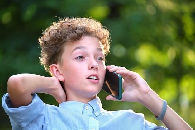 Young boy having an argument while talking on cellphone outdoors in summer park. Conflict situations in teenage years concept