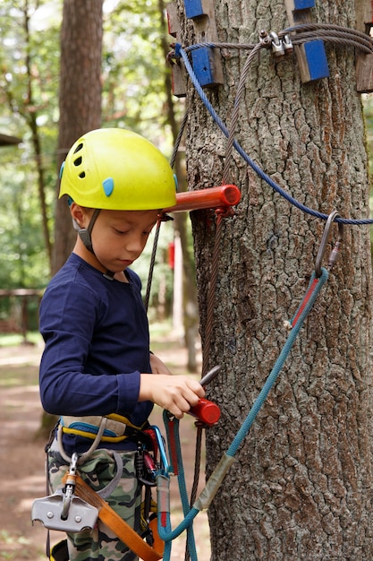 Young boy in helmet spend his leisure time in adventure playground.