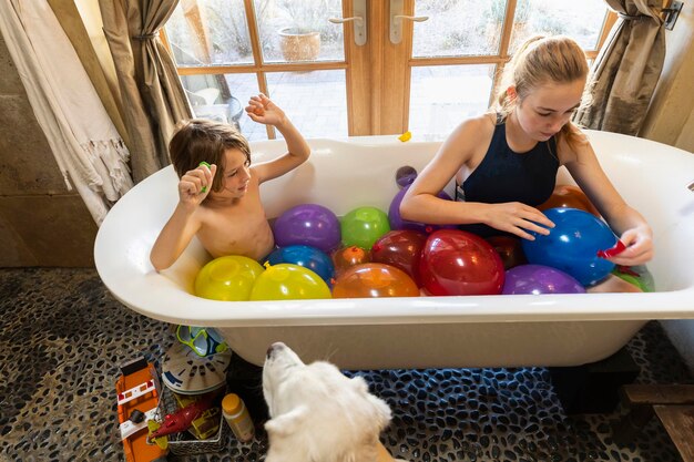 Photo young boy and his older sister in bathtub filled with water balloons