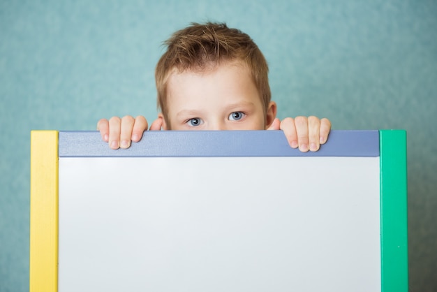 青い背景に白い空白のボードを保持している少年