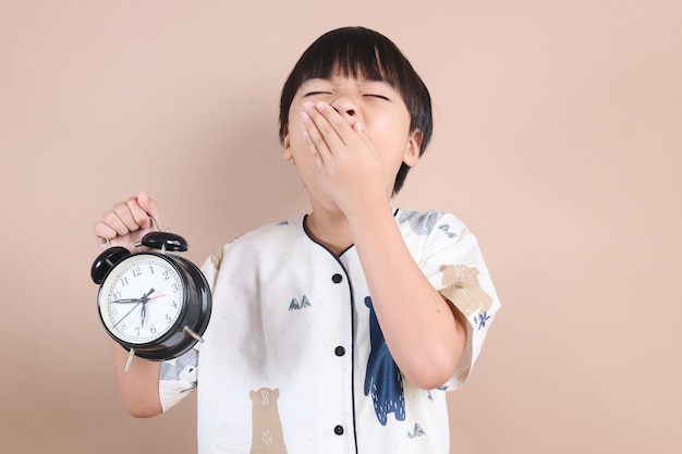 사진 잠옷 을 입은 어린 소년 은 깨어나야 할 시간 을 는 동안 알람 시계를 보여 준다