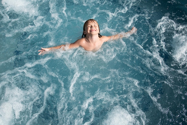 Young boy kid child splashing in swimming pool having fun leisure activity open arms