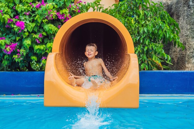 Photo young boy or kid has fun splashing into pool after going down water slide during summer