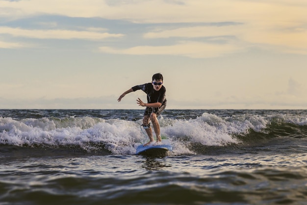 Photo young boy kid surfer riding waves with a soft board in rayong beach thailand rookie surfboard student playing on water in excited face and funny action