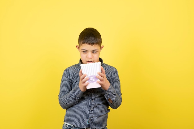 young boy looking inside of box of popcorn over yellow.