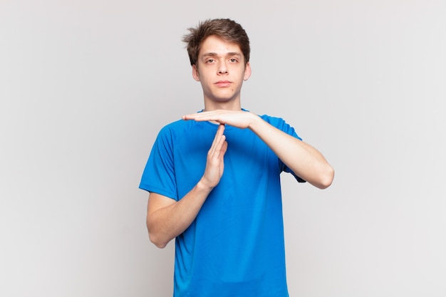 Young boy looking serious, stern, angry and displeased, making time out sign