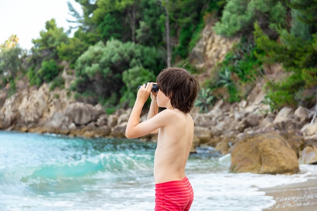 A young boy looking through binoculars staying at the seaside on the beach.