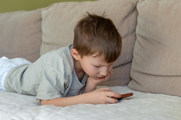 Young boy lying on couch using smartphone a young boy lies on a cozy couch deeply focused on his