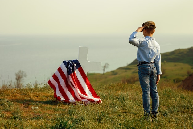 A young boy in a military cap salutes his father's grave on memorial day
