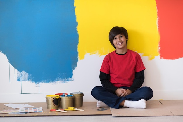 새 집 바닥에 앉아 벽을 칠한 후 쉬고 있는 어린 소년 화가