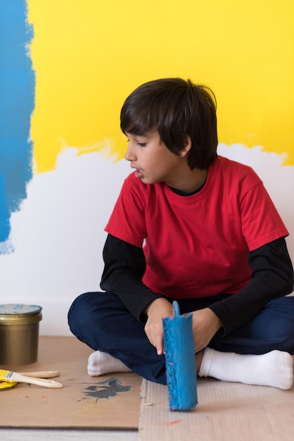 young boy painter resting after painting the wall, sitting on the floor in new home