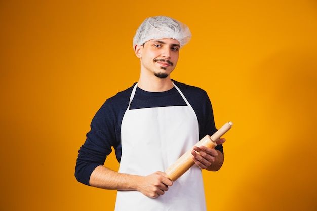 Young boy pizza maker on yellow background holding rolling pin.