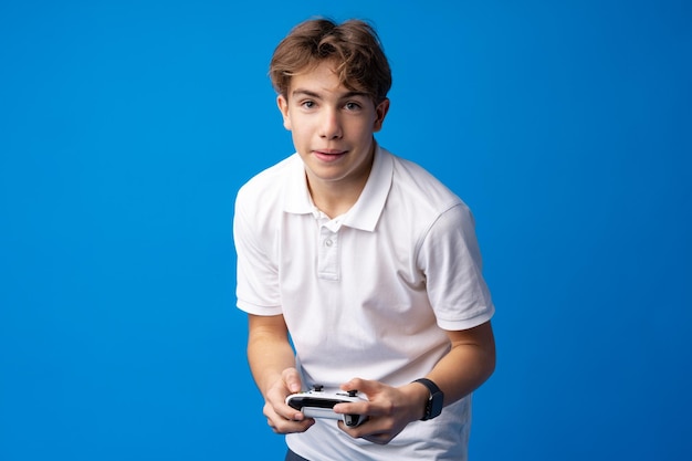 Young boy playing computer games with jojystick against blue background