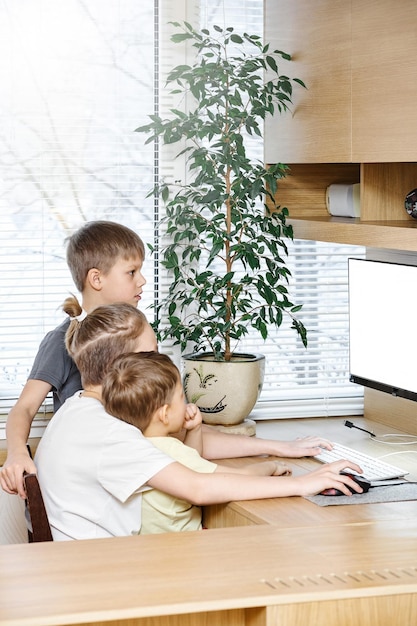 Young boy pupils sit on chair at wooden computer desk looking into white monitor