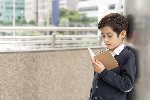 Giovane ragazzo che legge un libro sul distretto aziendale urbano, concetto di istruzione