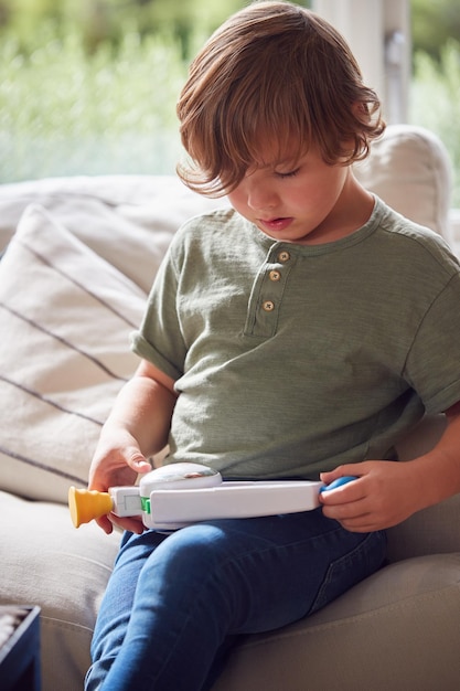 Young Boy Relaxing On Sofa At Home Playing With Toy