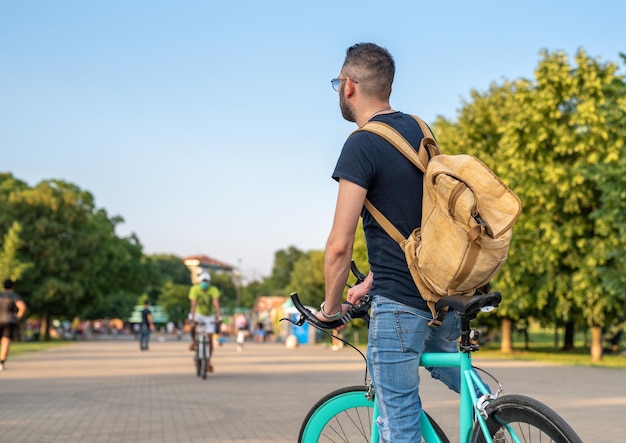 後ろから見た少年、ミニマリストの自転車に立って、バックパックを身に着けて、都市と公園の都市と生態系のモビリティの概念