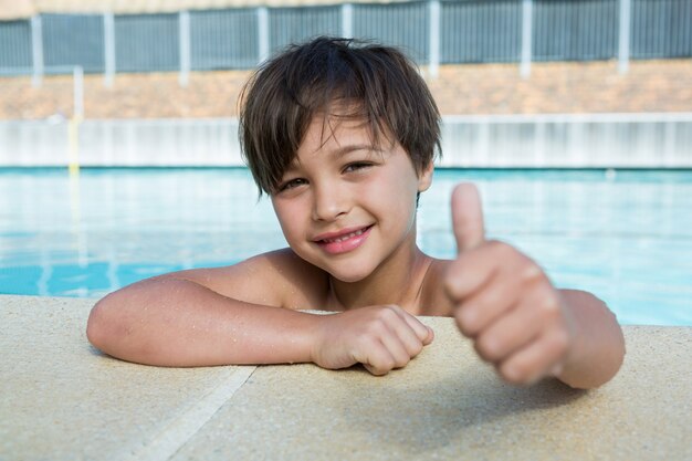 Young boy showing thumbs up at poolside