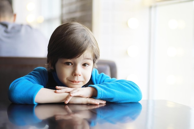 A young boy sits at a table near the window in a cafe and waits for a waiter to come up and take an order.