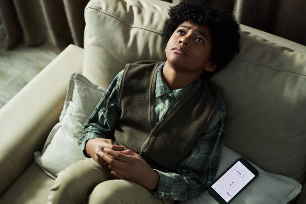 young boy sitting on couch with smartphone by his side