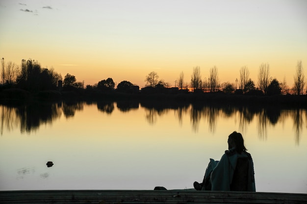 その色で夕日を見ながら湖の前に座っている少年