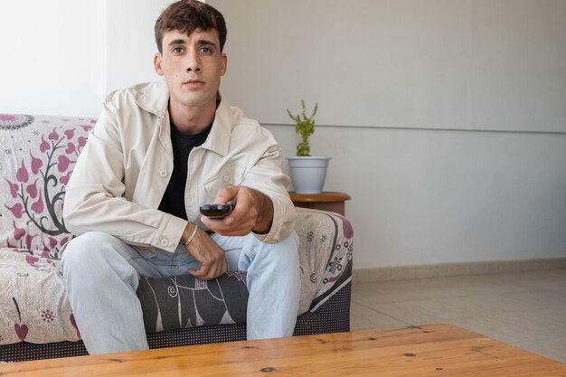 Photo young boy sitting on the sofa looking for a movie with the remote control