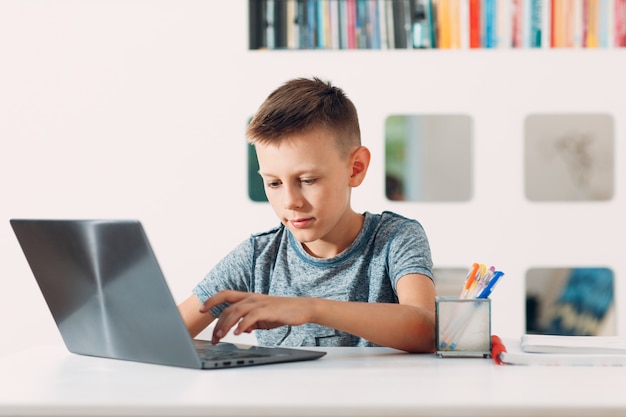 young boy sitting at table with laptop and preparing to school online education schoolboy concept