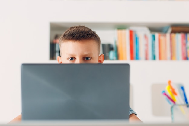 Young boy sitting at table with laptop and preparing to school