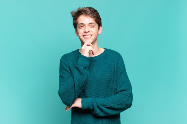 Young boy smiling, enjoying life, feeling happy, friendly, satisfied and carefree with hand on chin