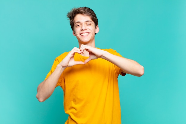 Young boy smiling and feeling happy, cute, romantic and in love, making heart shape with both hands